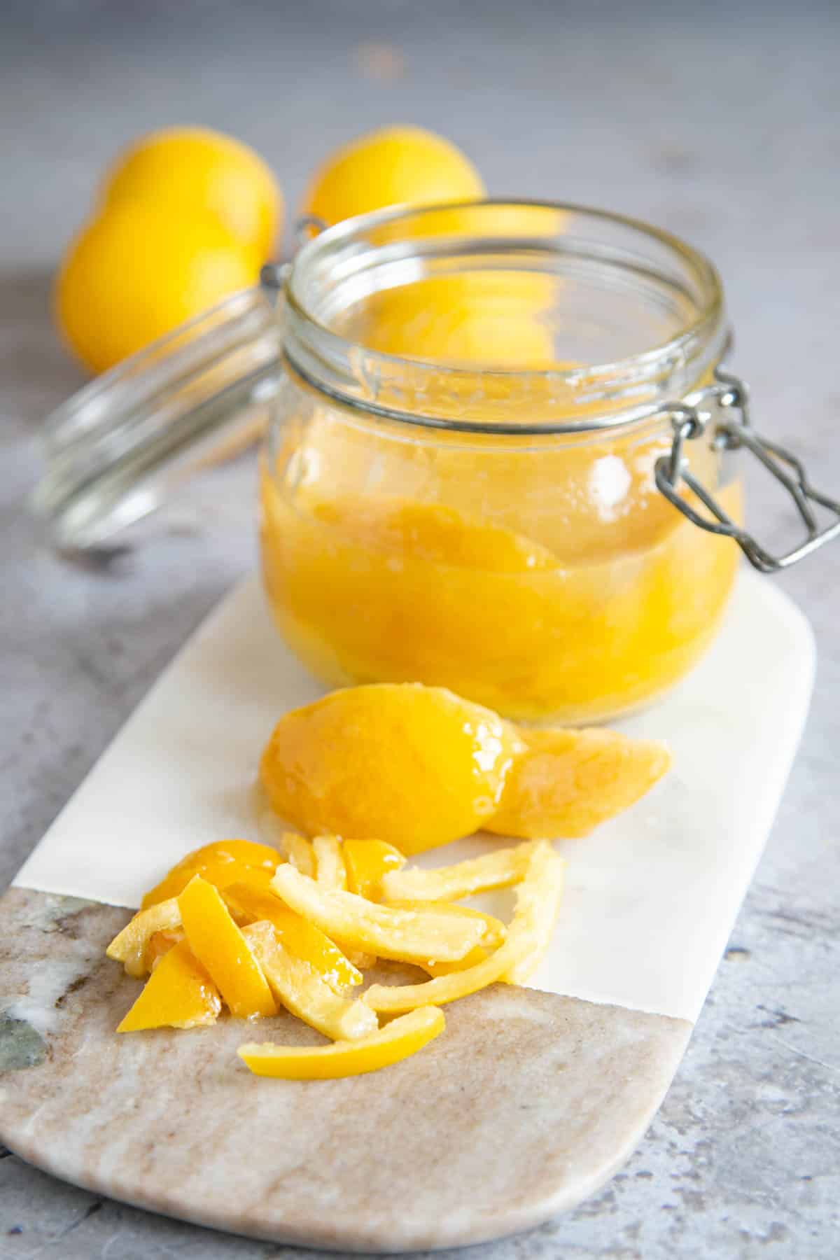 An open jar of preserved next to a chopped preserved lemon on a marble board.