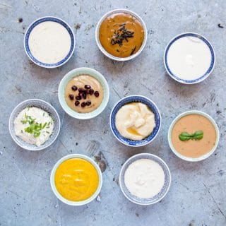 8 small bowls of tahini dressing on a discressed metal background viewed from above.