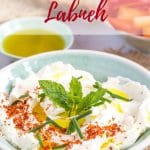 A shallow green bowl of fresh labneh, topped with a pinch of chili flakes, finely chopped chives, a sprig of mint and a slurp of olive oil. In the background are slices of bread, carrot stick and slice peppers in a bowl, and a small dish of olive oil. Text overlay reads how to make labneh