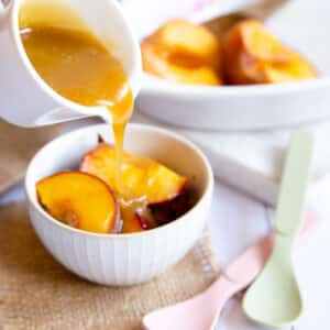 Delicious roast peaches in a simply but pretty serving bowl, drizzled with butterscotch sauce