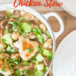 A white casserole dish filled with a chicken stew, with large pieces of borwned chicken, mushrooms and green leeks viewed from above. Test overlay reading Simple French Chicken Stew