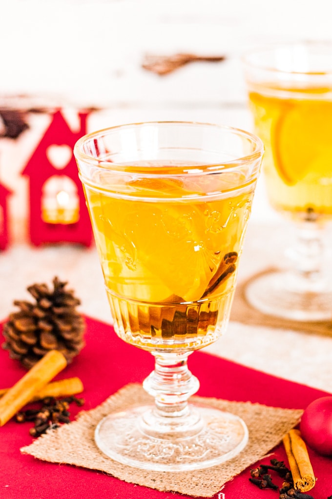 A glass of mulled cider garnished with a slice of orange and a cinnamon stick