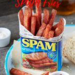 A SPAM can lied with newspaper and filled with crispy SPAM fries. Standing on a whie and blue tray, with a few fries scattered about with a small bowl of tomaot ketchup. Text overlay reading SPAM fries