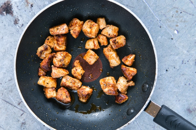 A top down view of a black frying pan holding cubes of spicy garlic chicken. The chicken has been cooked, and is coloured brown.