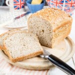 Two slices and a loaf of bread made with leftover oatmeal on a bread board on a table set for breakfast with a Union Jack teapot and mug