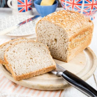 Two slices and a loaf of bread made with leftover oatmeal on a bread board on a table set for breakfast with a Union Jack teapot and mug