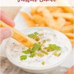 A crisp thick cut chip dipping into a small dish of pale tartare sauce