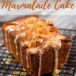 A delicious, sticky orange marmalade loaf cake dripping with marmalade drizzle sitting on a wire cooling rack. Text overlay reads Orange Marmalade Cake