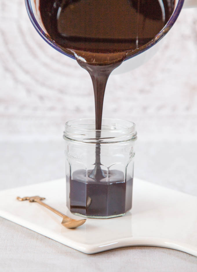 dark and itnense 2 ingredient vegan chocolate sauce pouring into a jar from the pan