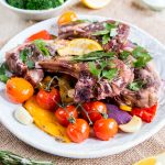 A plate of colourful roast Mediterranean vegetables, topped with roast lamb chops and garnished with parsley.