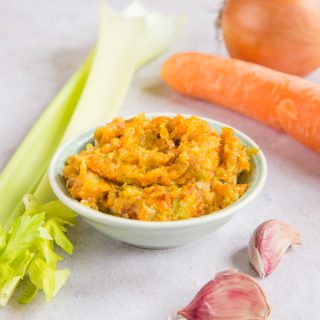 A small dish of soffritto paste together with its main ingredients: carrot, onion, garlic and celery.