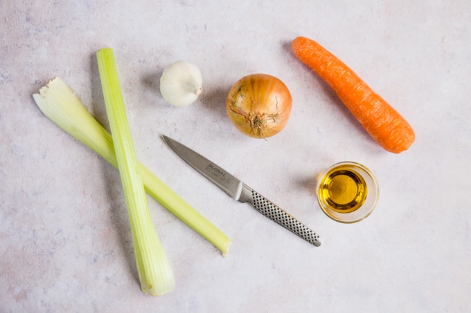 Raw celery, garlic, onion and carrot with a knife and a small glass of oil. The first stage of making soffritto.