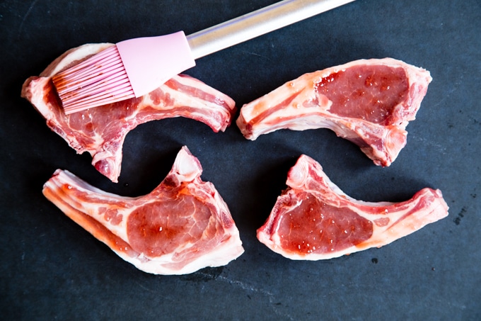 Brushing a Worcestershire Sauce and redcurrant jelly glaze onto four lamb chops on a board.