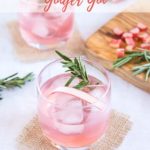 Two glasses containing pink rhubarb and ginger gin, ice cubes and a sprig of resemary. In the backbround there is a wooden chopping board with chopped rhubarb and some more rosemary. Text overlay reading Rhubarb and ginger gin