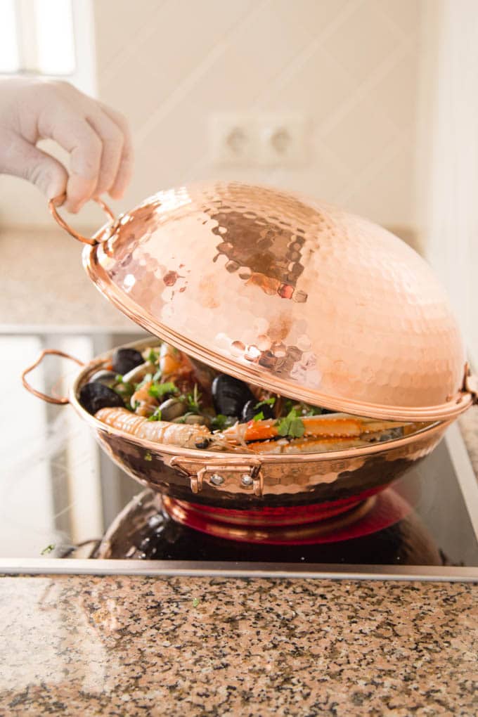 A traidiotnal Portuguese copper cataplana pan filled with seafood with the domed lid being lowered.