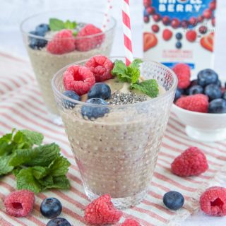 A pale green glass of cranberry smoothie with pea and avocado, topped with raspberries, blueberries, chia seeds and mint, ready to be enjoyed through a striped straw.
