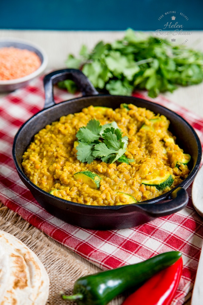 A dish of zucchini or courgette daal, on a red and white gingham napkin. Chilis in the foreground, lentils and a handful of coriander in the background.
