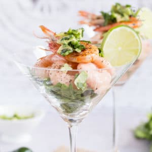 Close up on a retro prawn cocktail, in a traditional cocktail glass. Garnished with a cooked prawn and a slice of lime.