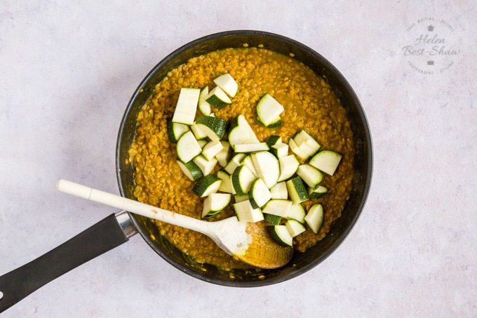 A frying pan of orange daal, topped with chopped courgette.