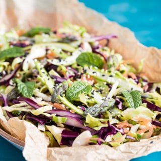 Colourful and flavourful asparagus coleslaw salad served on greaseproof paper, placed in a shallow wooden bowl, topped with a lemon juice and balsamic vinegar dressing, and garnished with fresh mint leaves.