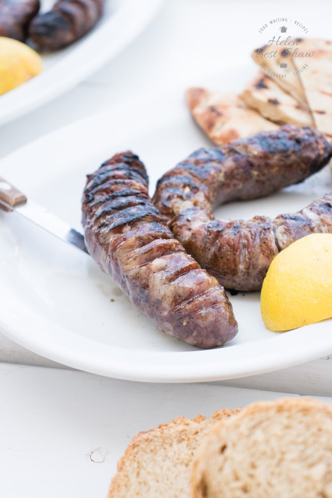 A white plate with two grilled sausages served with a wedge of lemon