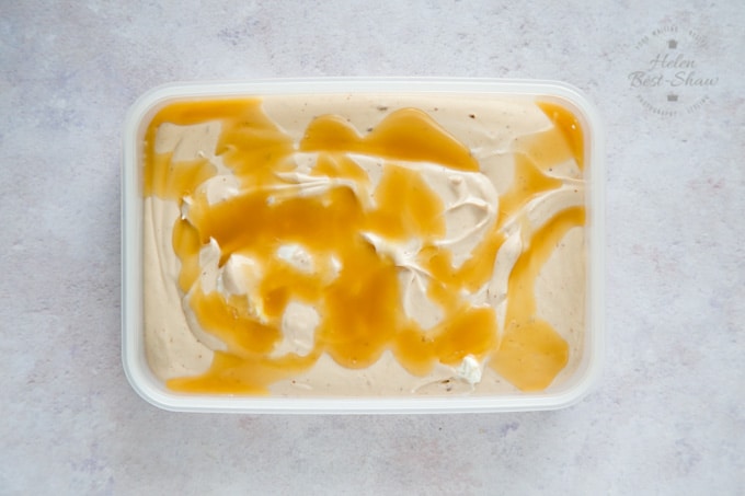 A top down view of the rectangular container full of no-churn Twix ice cream ready to be frozen. Caramel sauce has been drizzled on top, and lies in uneven pools.