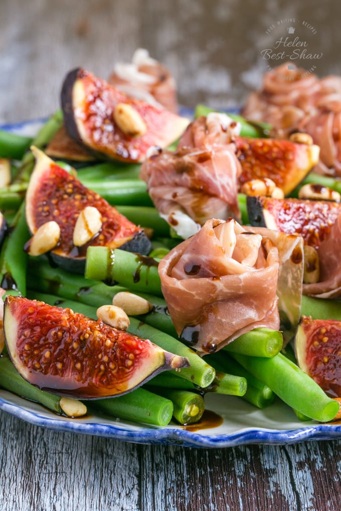 A close up shot of a plate of Parma ham salad served with green beans and figs