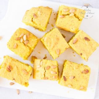 A top down view of eight square slices of yellow sfoof turmeric cake on a white square porcelain board.