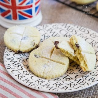 A picture of a sideplate holding four soul cakes: golden biscuits with crosses cut into the top. One has been broken in two, and you can see raisins in the middle. Out of focus towards the back of the picture is a small Union Jack mug.