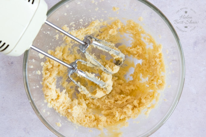 A picture from above of a glass bowl with electric beaters mixing together sugar and butter.