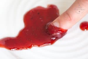 A close up of some jam on a saucer. A finger is pushing through the sauce to check the setting point.