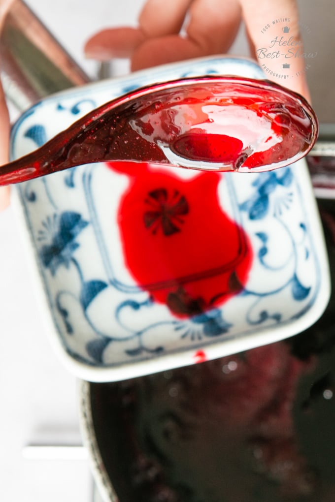 A teaspoon of jelly held above a small square dish, to see how the jelly drips off the dish and test the setting point.