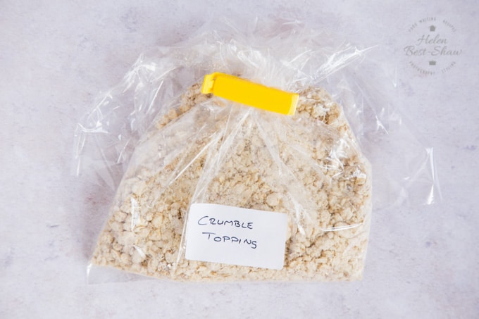 A shot of a plastic bag full of crumble topping, ready for storing in the freezer. The bag has been labelled with a hand-written label, and it’s closed with a yellow clip. 