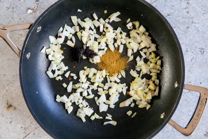 Making Mexican refried beans: a top down picture of a large black frying pan holding a mixture of fried onions to which spices have been just added.