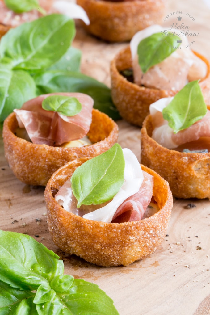 A close up of Parma ham canapes with sticky balsamic onion, with and gorgonzola, garnished with basil leaves.