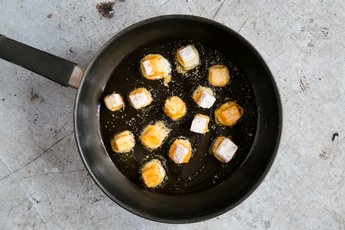 A frying pan with crispy cheese bites being cooked.