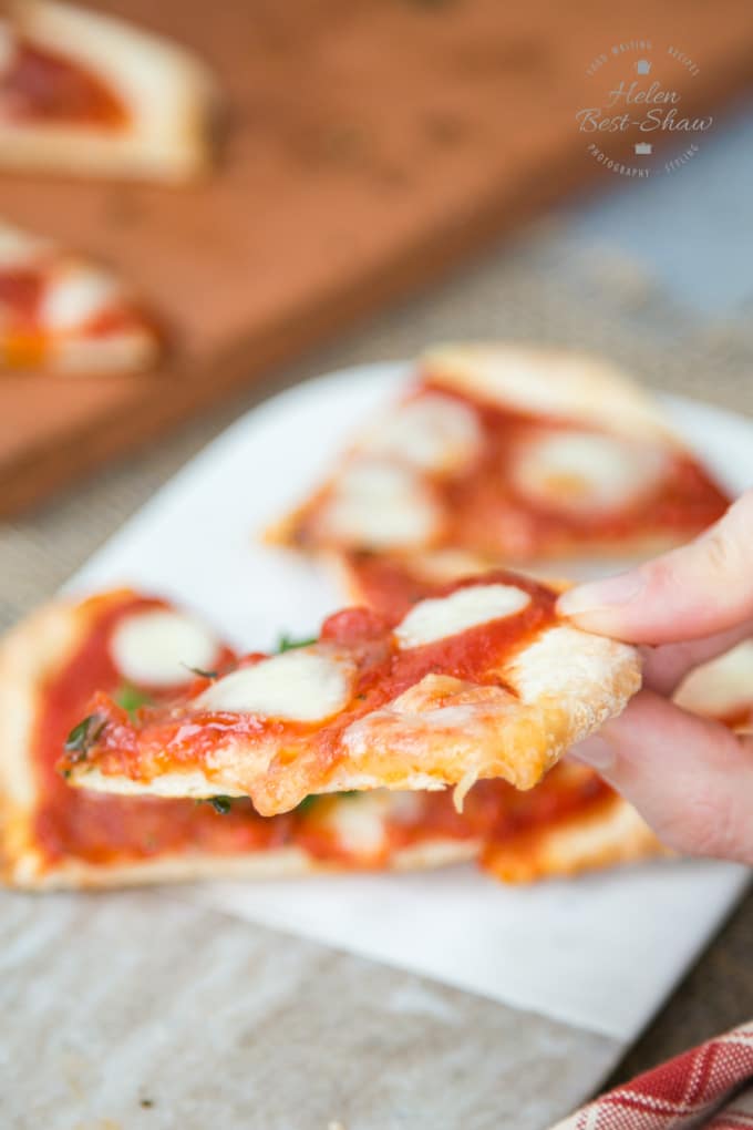 A picture of a hand holding a slice of no yeast pizza