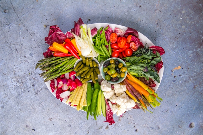 A top down view of an oval platter of raw vegetable crudités of all colours.
