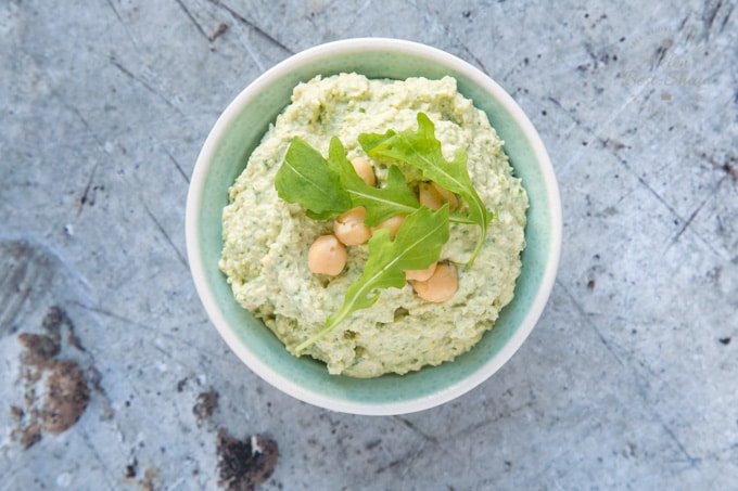 A top down view of a dish of goats cheese and rocket hummus, garnished with rocket leaves and chickpeas.