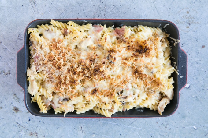 A top down view of a black rectangular dish full of turkey and ham pasta bake. The dish has been cooked, and the topping of breadcrumbs and cheese has browned in the oven.