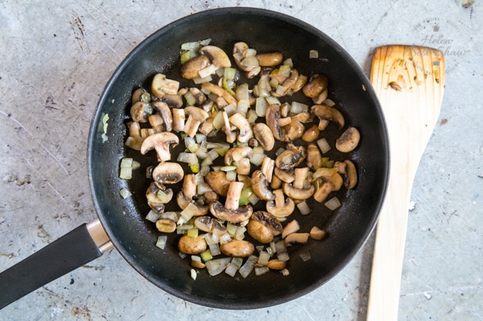 A picture of a frying pan holding chopped onions and sliced mushrooms. The onions have been cooked until translucent, and the mushrooms are browned.