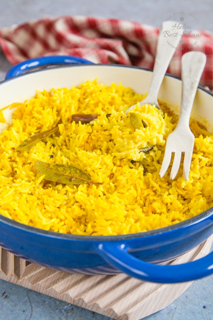 a casserole dish containing vibrant yellow home-made pilau rice. There are some cardamom pods, a stick of cinnamon and a bay leaf in the rice