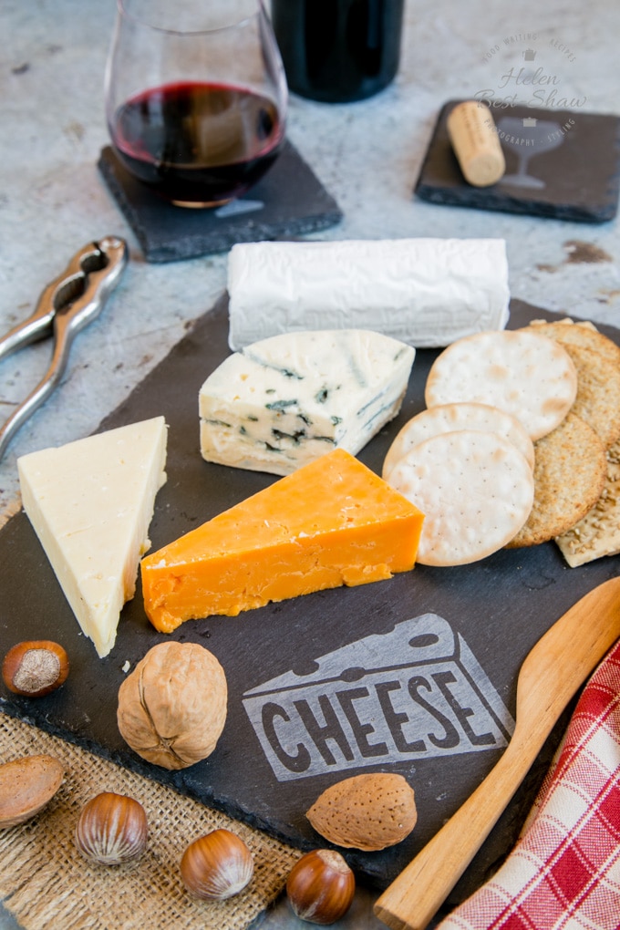 A lifestyle photo of an etched slate cheeseboard covered wtih a selection of cheeses