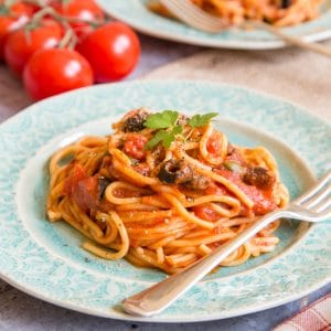 Rich red spaghetti puttanesca on a pale green plate.