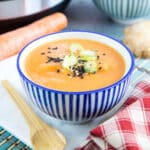 A bowl of quick and easy pressure-cooker carrot lentil soup, the rich orange of the soup contrasting with a blue and white bowl.