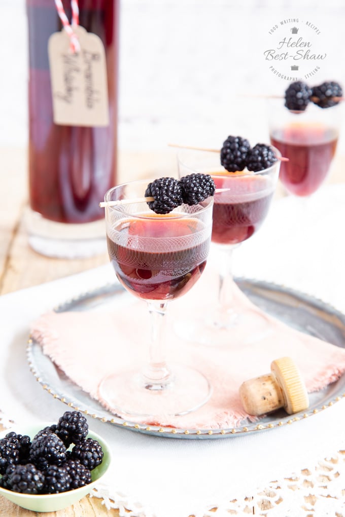 Three liqueur glasses of bramble whisky, garnished with blackberries, on a small tray.