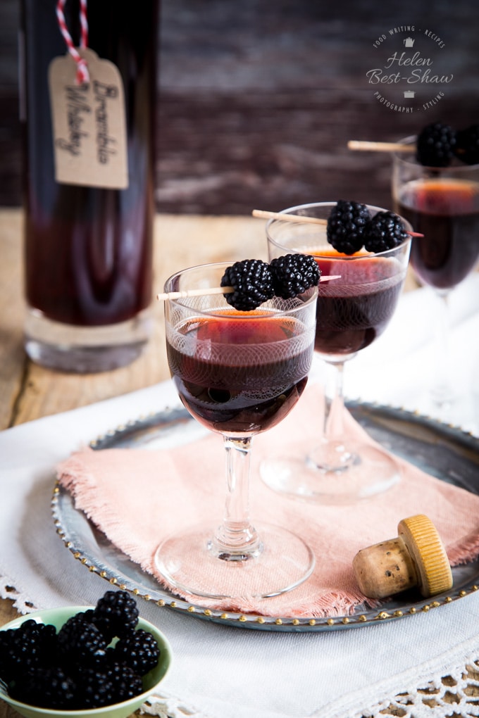 Two glasses of bramble whisky garnished with blackberries on cocktail sticks.
