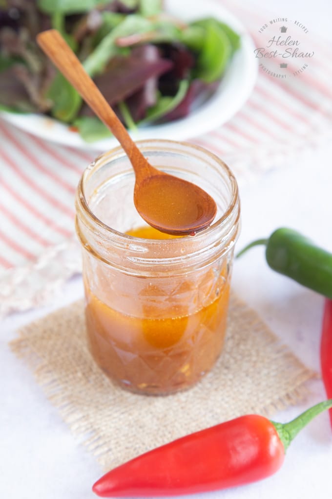 An open jam jar of sweet chilli sauce dressing, with a spoon balanced on top