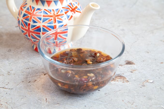 A bowl of dried fruit covered with tea. A union jack tea pot is behind the bowl