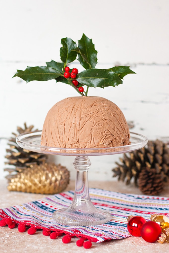 A chocolate Baileys ice cream bombe on a glass cakestand, surrounded by decorations.